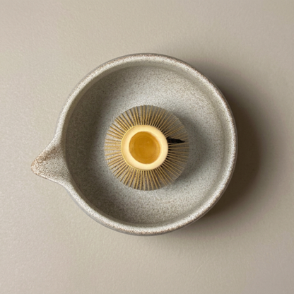 Top view of a golden bamboo matcha whisk with its hollow handle facing upward inside a speckled ceramic bowl.