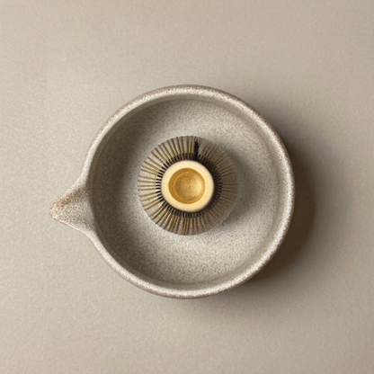 Top view of a purple bamboo matcha whisk inside a speckled ceramic bowl.