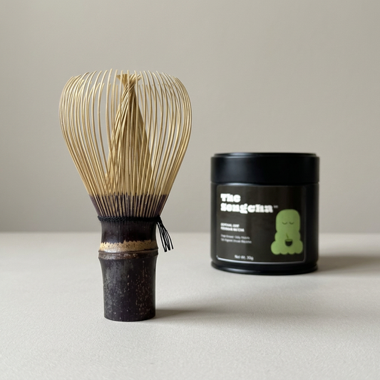Purple bamboo matcha whisk beside a black TheSongcha matcha 007 tin.